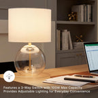 Signature Design by Ashley Glass Table Lamp, Modern Bedside, Clear & Brass | White fabric drum shade, Compact round clear glass profile for modern nightstands, Samder Series