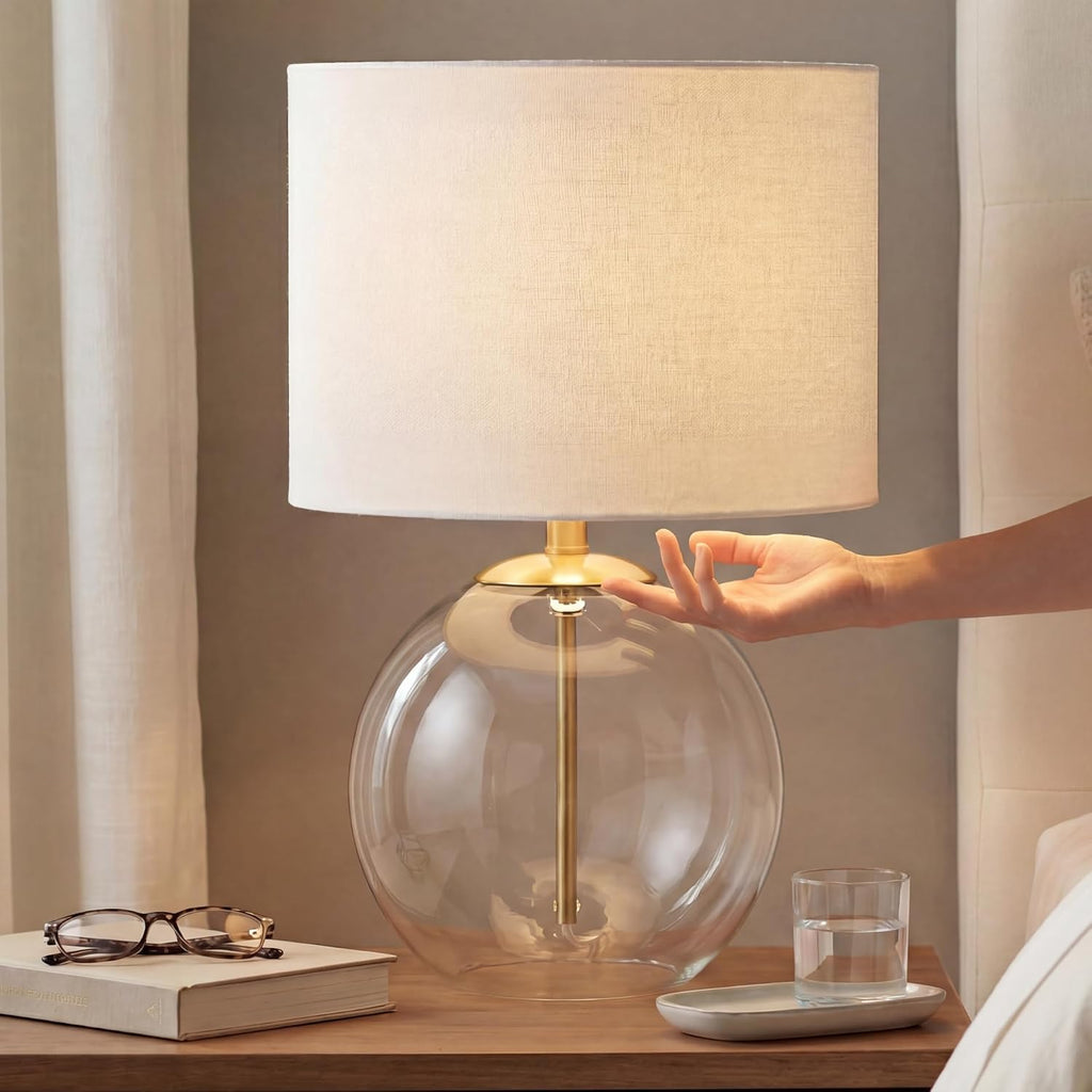 Signature Design by Ashley Glass Table Lamp, Modern Bedside, Clear & Brass | White fabric drum shade, Compact round clear glass profile for modern nightstands, Samder Series